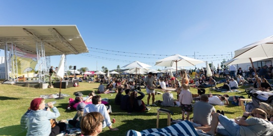 A crowd of people sitting outside the amphitheatre on a sunny day enjoying an event being held at the MET.